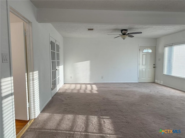 spare room with a textured ceiling, carpet flooring, visible vents, baseboards, and a ceiling fan