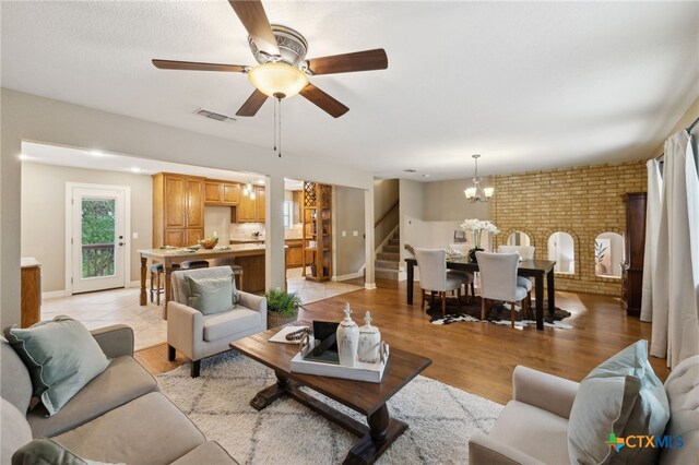 95 Mission Dr, New Braunfels, TX 78130 - living area with ceiling fan with notable chandelier, brick wall, visible vents, baseboards, and stairs