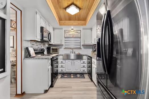 2305 Canyon Creek Dr, Temple, TX 76502 - kitchen with fridge with ice dispenser, black / electric stove, wooden ceiling, white cabinetry, and light wood-style flooring