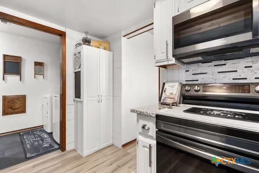 2305 Canyon Creek Dr, Temple, TX 76502 - kitchen with appliances with stainless steel finishes, light wood-type flooring, washer and dryer, white cabinets, and light countertops