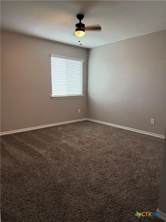 unfurnished room featuring dark carpet, a ceiling fan, and baseboards