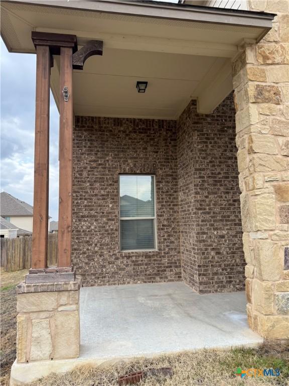 doorway to property with stone siding, fence, and brick siding