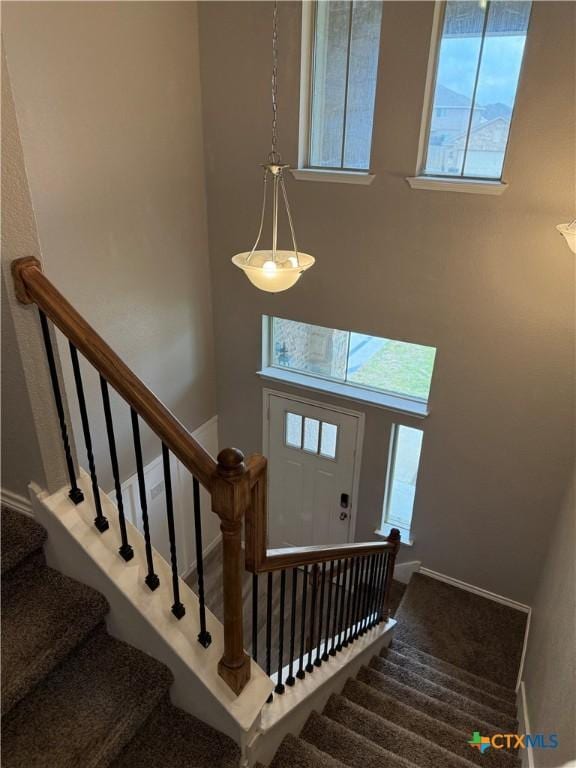 stairway with carpet flooring, a towering ceiling, and baseboards