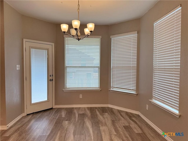 unfurnished dining area featuring a chandelier, baseboards, and wood finished floors