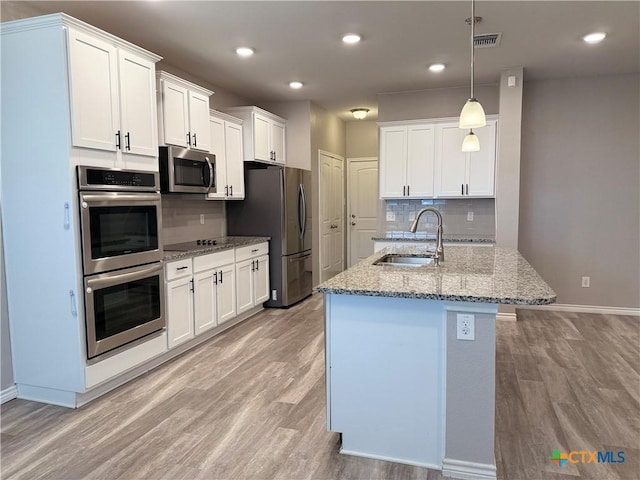 kitchen featuring stainless steel appliances, a sink, white cabinetry, light wood-type flooring, and light stone countertops