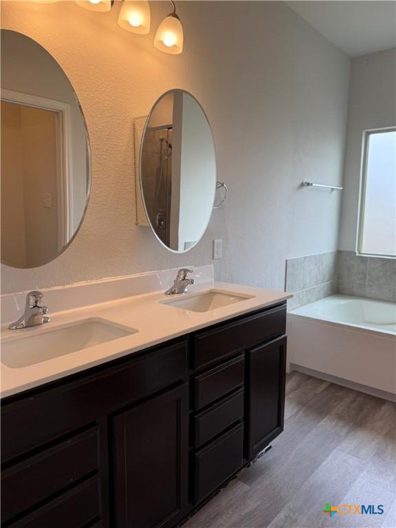 bathroom featuring double vanity, a bath, a sink, and wood finished floors