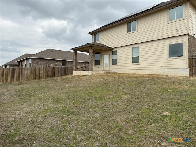 back of property featuring roof mounted solar panels, fence, and a lawn