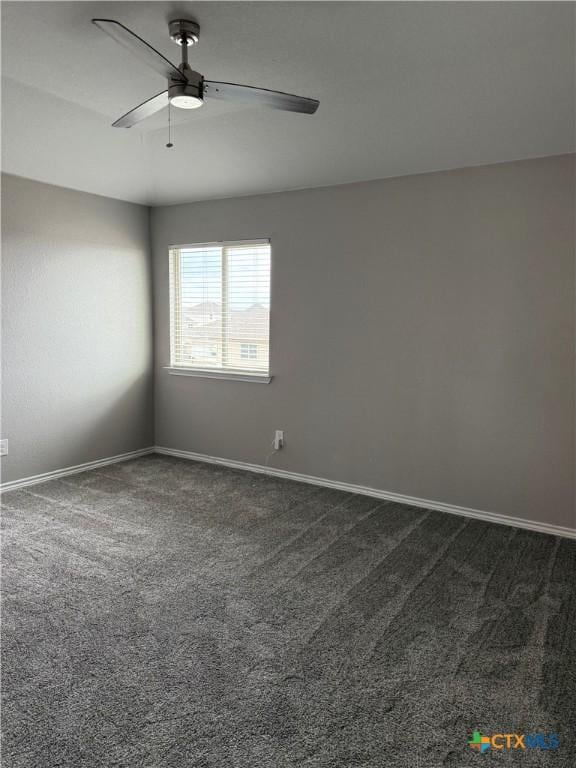 spare room featuring ceiling fan, dark colored carpet, and baseboards