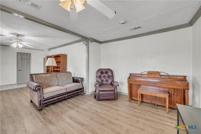 living room with ceiling fan, light hardwood / wood-style flooring, ornamental molding, and a textured ceiling