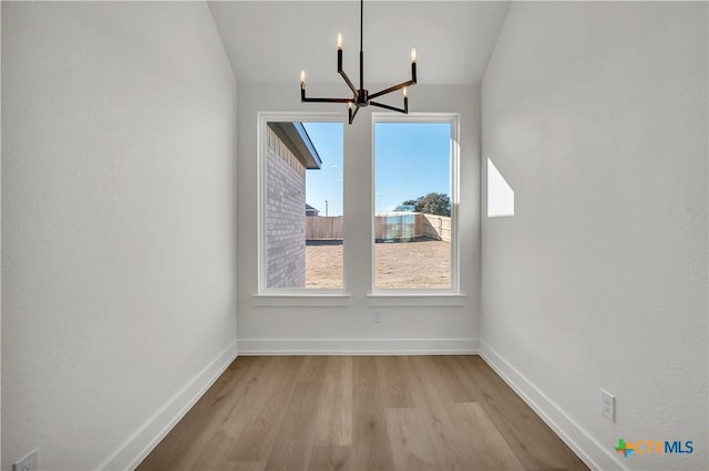 unfurnished dining area with an inviting chandelier and light wood-type flooring