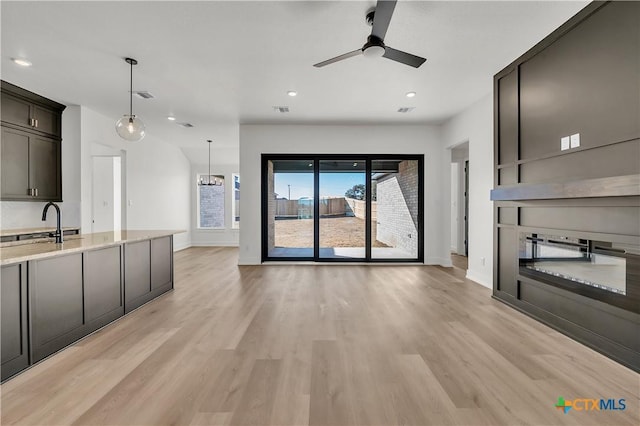 unfurnished living room with ceiling fan, sink, a fireplace, and light hardwood / wood-style floors