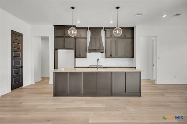 kitchen with sink, decorative light fixtures, custom range hood, and an island with sink