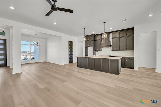 kitchen featuring ceiling fan with notable chandelier, light hardwood / wood-style floors, an island with sink, and hanging light fixtures