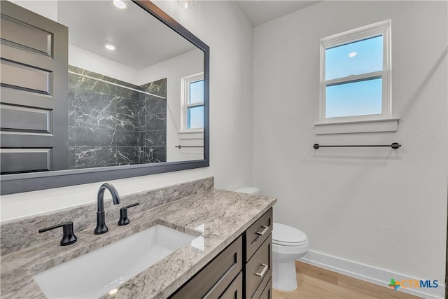 bathroom featuring vanity, wood-type flooring, toilet, and tiled shower