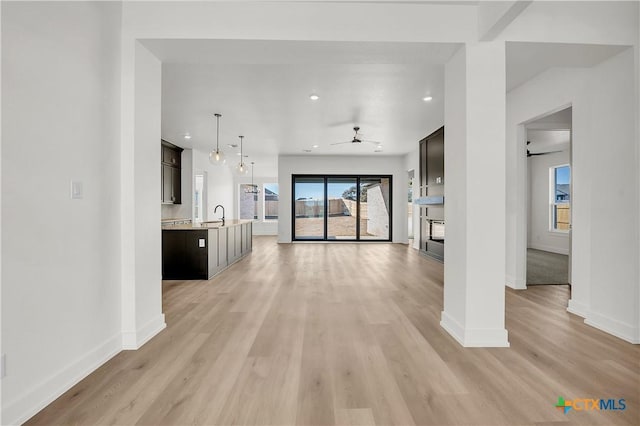 unfurnished living room with ceiling fan, sink, a fireplace, and light hardwood / wood-style flooring