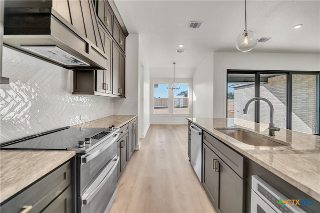 kitchen featuring dark brown cabinetry, sink, appliances with stainless steel finishes, custom range hood, and pendant lighting