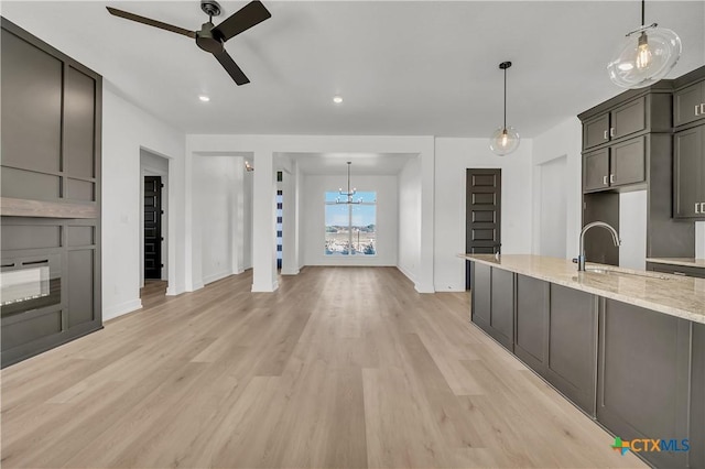 kitchen with sink, hanging light fixtures, light stone counters, light hardwood / wood-style floors, and ceiling fan with notable chandelier