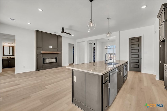 kitchen featuring sink, decorative light fixtures, a center island with sink, stainless steel dishwasher, and a large fireplace