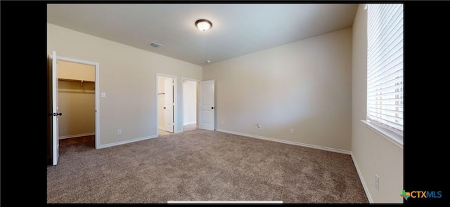 unfurnished bedroom featuring visible vents, carpet floors, baseboards, and a walk in closet