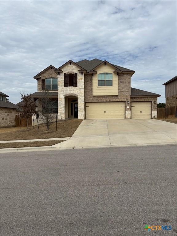 view of front of property with driveway, stone siding, fence, a garage, and brick siding