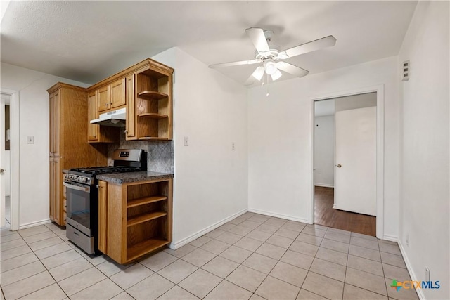 kitchen with light tile patterned floors, under cabinet range hood, stainless steel range with gas cooktop, open shelves, and dark countertops