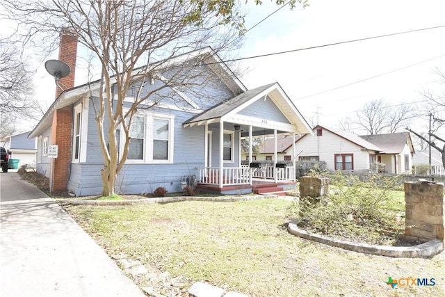 bungalow featuring a porch, a chimney, and a front lawn