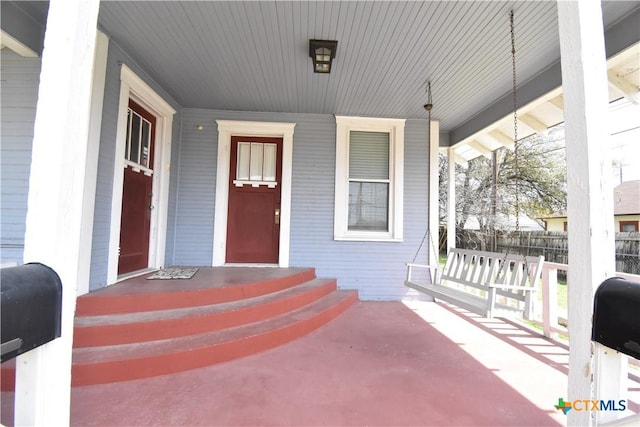 view of exterior entry with a porch and fence