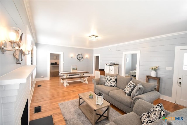 living room with crown molding, light wood-style flooring, and visible vents