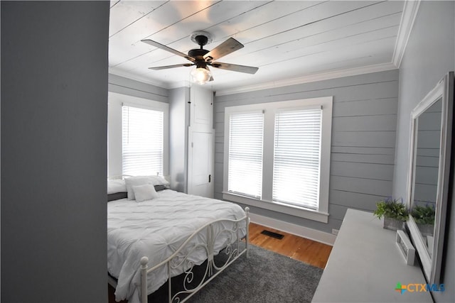 bedroom with visible vents, wood finished floors, baseboards, and ornamental molding