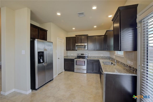 kitchen featuring stainless steel appliances, tasteful backsplash, sink, light stone counters, and dark brown cabinets