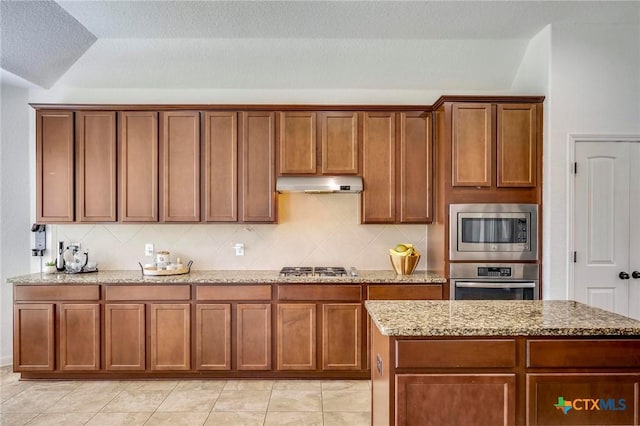 kitchen featuring appliances with stainless steel finishes, light stone countertops, a textured ceiling, and decorative backsplash