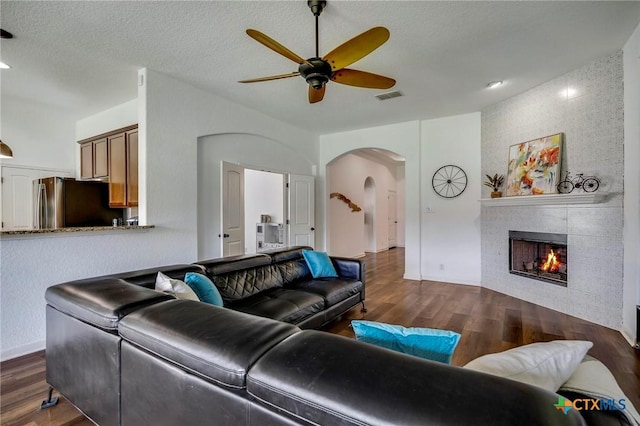 living room featuring ceiling fan, a tiled fireplace, dark wood-type flooring, and a textured ceiling