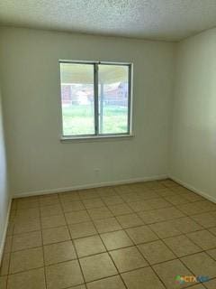 tiled empty room featuring a textured ceiling