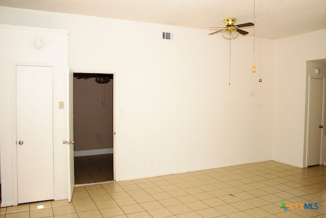 empty room with ceiling fan, light tile patterned floors, and a textured ceiling