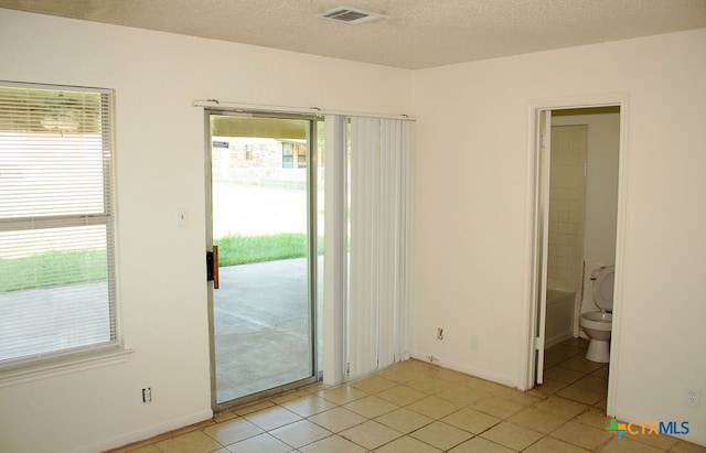 spare room featuring plenty of natural light, light tile patterned floors, and a textured ceiling