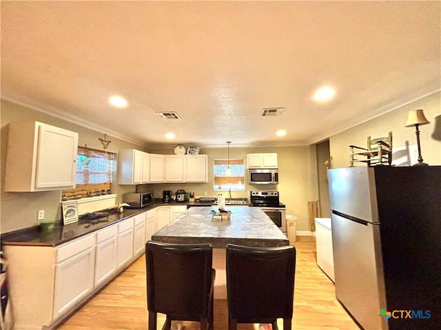 1306 W Madison Ave, Port Oconnor, TX 77982 - kitchen with stainless steel appliances, ornamental molding, a center island, white cabinetry, and light wood finished floors