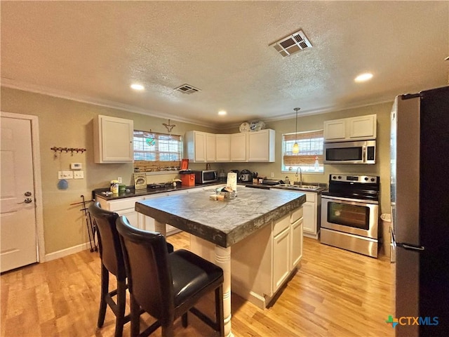 1306 W Madison Ave, Port Oconnor, TX 77982 - kitchen featuring stainless steel appliances, ornamental molding, healthy amount of natural light, white cabinetry, and a kitchen island