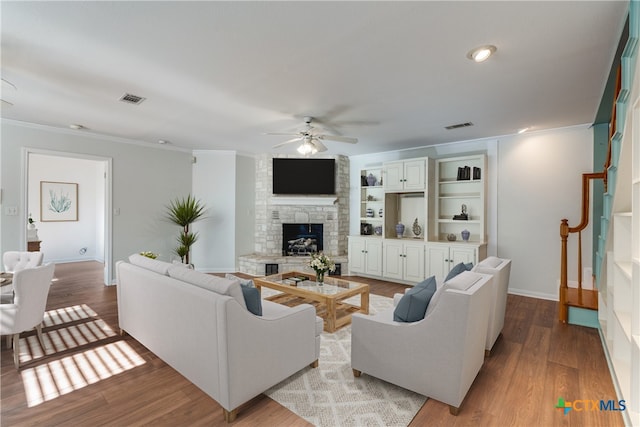 living room with light hardwood / wood-style floors, a stone fireplace, ceiling fan, and ornamental molding