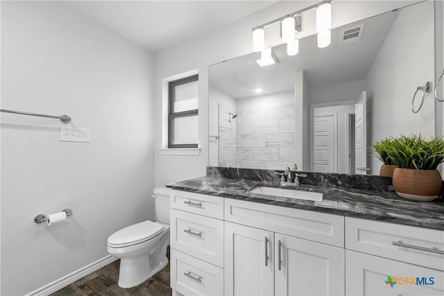 bathroom with wood-type flooring, a tile shower, vanity, and toilet