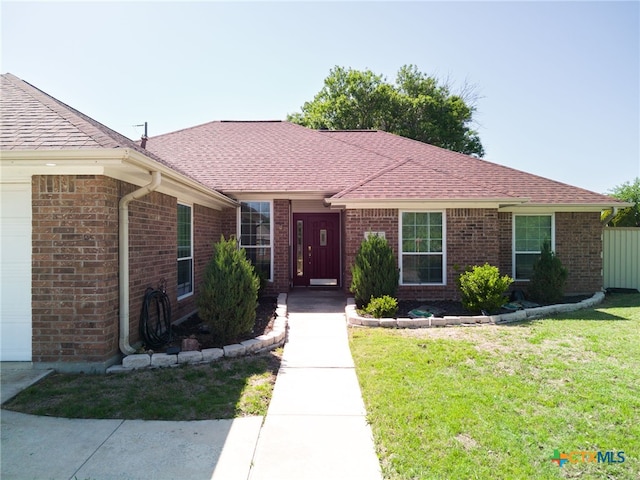 single story home featuring brick siding, a front yard, an attached garage, and roof with shingles