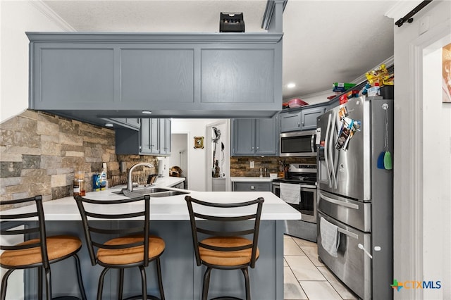 kitchen with stainless steel appliances, a peninsula, a sink, decorative backsplash, and gray cabinetry