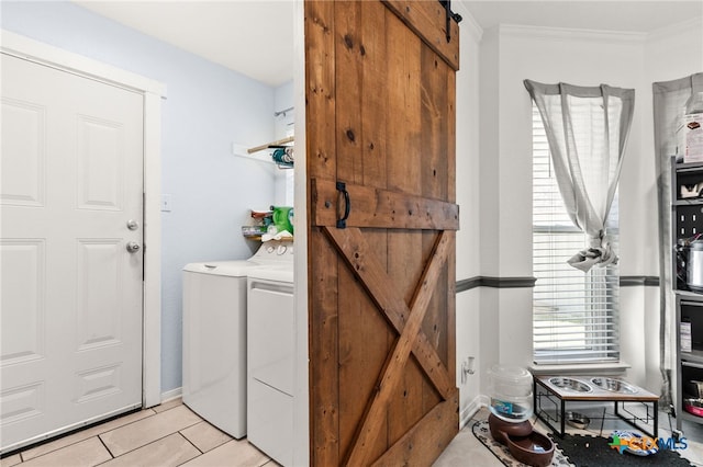 washroom featuring washing machine and dryer, a barn door, light tile patterned flooring, crown molding, and baseboards