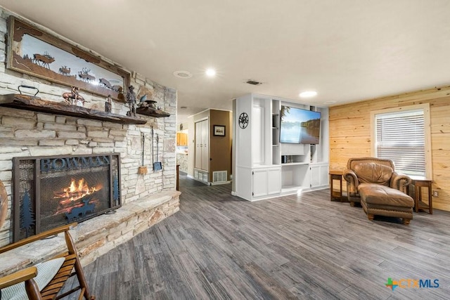 living room with dark hardwood / wood-style floors, wood walls, and a stone fireplace