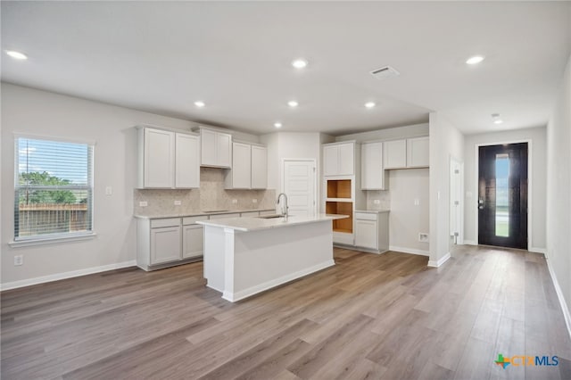 kitchen with white cabinets, light wood-type flooring, a kitchen island with sink, and sink