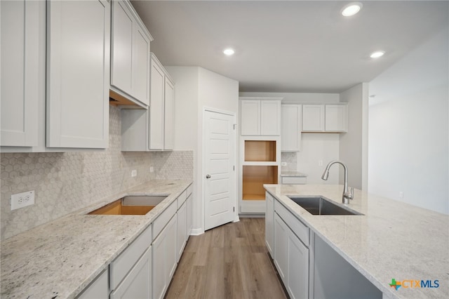 kitchen featuring light stone countertops, sink, white cabinets, and light wood-type flooring