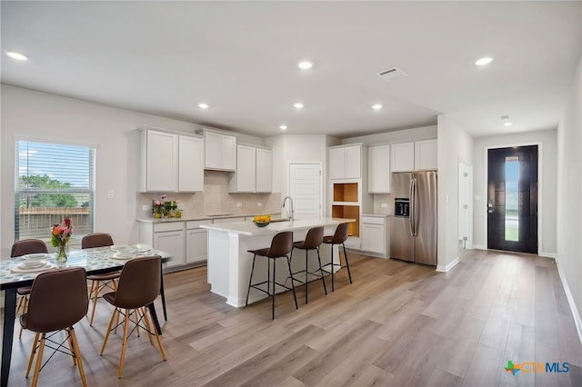 kitchen featuring stainless steel refrigerator with ice dispenser, light wood-type flooring, a center island with sink, and white cabinetry
