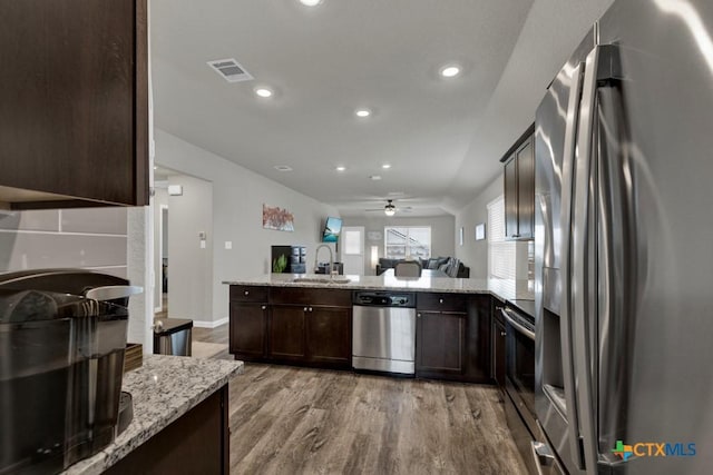 kitchen featuring visible vents, a peninsula, a sink, stainless steel appliances, and dark brown cabinetry