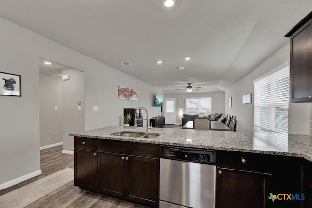 kitchen with light stone counters, dark brown cabinetry, dishwasher, and a sink