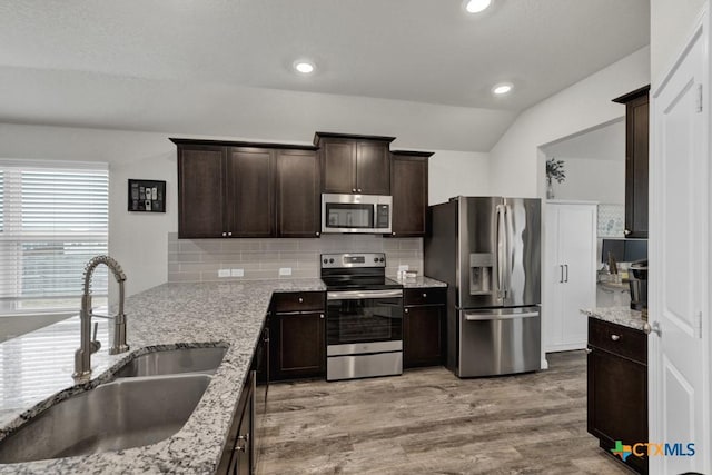 kitchen with light wood finished floors, tasteful backsplash, dark brown cabinets, appliances with stainless steel finishes, and a sink