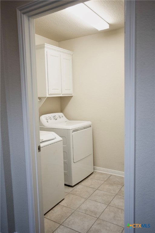 laundry area featuring washing machine and dryer, cabinets, and light tile patterned floors